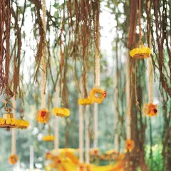 A daytime view of the hanging decor from a banyan tree. This setup features delicate floral rings and tassels made of marigolds, creating a whimsical and natural ceiling for an outdoor event.