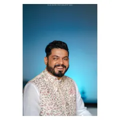 A portrait of the groom, ready for the big day. The clean background and soft lighting highlight his smile and the fine floral pattern of his traditional wedding vest.