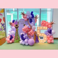 A fairytale come to life for a 5th birthday with our Rapunzel theme. This setup includes a large light-up number '5', a custom backdrop with Princess Avah's name, a Rapunzel tower cutout, and a flowing balloon garland in shades of purple and pink with golden starburst accents.