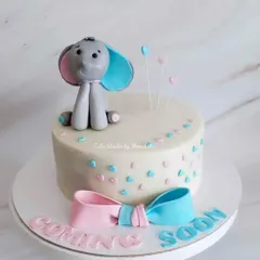 A cute baby shower cake with a "Coming Soon" message. This design features a sweet elephant topper and a pink and blue bow to keep the gender a surprise.