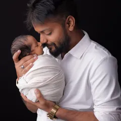 The powerful bond between a father and his newborn child. He holds his baby close, nose-to-nose, in a simple yet profound gesture of love. The dark background makes this intimate moment the sole focus.