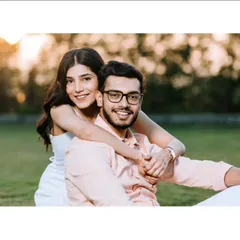 A warm and joyful portrait taken during golden hour. The woman embraces her partner from behind, both smiling at the camera, creating a photo that feels both posed and genuinely happy.