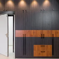 This floor-to-ceiling hinged wardrobe features a bold two-tone design with dark wood grain and a lighter wood accent band. The long metal handles and overhead spotlights add to its modern, sophisticated feel.