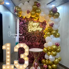 For a teenager's party, this pink shimmer wall backdrop creates a fun and stylish photo corner. The setup includes a 'Happy Birthday' neon sign, a light-up number '13', and a balloon garland in white, gold, and pink.