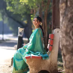 A serene moment captured on a park bench. The bride's natural makeup and the beautiful drape of her saree create a picture of timeless elegance.