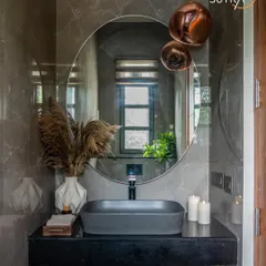A powder room that makes a statement. The design features a fluted wooden vanity, a matte black vessel sink, and dramatic copper pendant lights against moody grey marble walls for a look of sophisticated luxury.