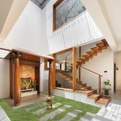 We believe every part of a home should be beautiful and functional. Here, a modern pooja room with traditional wooden pillars and a floating teak staircase coexist harmoniously, both illuminated by a double-height skylight that forms the spiritual and architectural heart of the home.