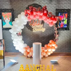 A stylish circular balloon arch in red, white, and rose gold, perfect for a modern birthday party. The arch is accented with butterfly details and a central neon sign.