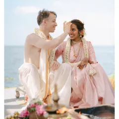 A tender moment during a seaside Hindu ceremony, as the groom applies a tilak to the bride's forehead. The sea behind them adds a sense of infinite possibility to their union.