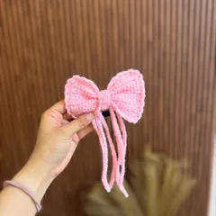 This adorable pink crochet bow comes with long tassels for a playful touch. It's attached to a hair tie for easy styling.
