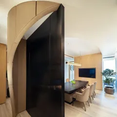 The curved, dark metal door of the conference room provides a strong contrast to the light wood paneling, creating a dramatic entryway into the meeting space.