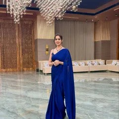 A solo shot in a beautiful blue saree at a grand event venue. Ready to mingle and host.