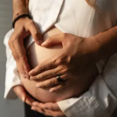 A symbol of love. The couple's hands form a heart shape on the baby bump, a simple yet profound gesture captured in a beautifully lit, close-up photograph.