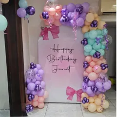 A beautiful pastel-themed birthday backdrop for Janet. The decoration includes an arched panel and a multi-colored balloon garland with purple, peach, and mint green tones.