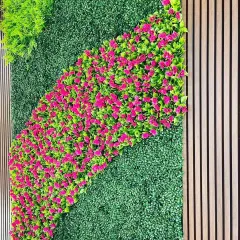 I can create artistic patterns with colorful artificial plants. This wall features a simple green base with a flowing wave of bright pink flowers, adding a pop of color to the design.