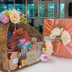 An elegant wedding hamper for a friend's special day. The gift includes a golden wire basket filled with curated items like a scented candle and Ferrero Rocher, paired with a Furoshiki-wrapped present.