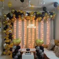 An elegant black and gold balloon garland for a birthday celebration. This setup includes a 'Happy Birthday' neon sign and a fairy light curtain, creating a sophisticated photo backdrop in the living room.