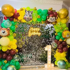 A closer look at the jungle safari theme backdrop. This setup combines a multi-colored balloon arch with foil animal heads like a zebra, monkey, tiger, and lion, set against a sparkling sequin wall for a fun photo corner.
