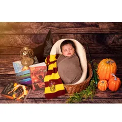 A magical Harry Potter scene comes to life with a sleeping baby in a basket, surrounded by books, a sorting hat, a magic wand, and pumpkins. It's the perfect setup for the newest little wizard.