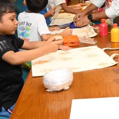 Children are gathered around a table filled with paints and art supplies, focused on their tote bag projects. We set up everything needed for the workshop, creating an organized yet playful environment for creativity to flourish.