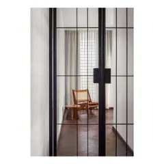 A glimpse through full-height pivot metal doors into a lounge area. We use architectural elements like these gridded doors to create visual connection and separation, adding a layer of industrial elegance to the home.
