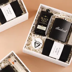 A closer look at our groomsmen gift box. It includes a miniature bottle of Black Dog, a personalized flask for Shashank, 'Team Groom' badge, and socks that say "It's time to suit up!".
