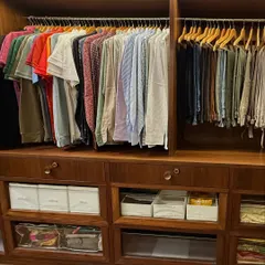 A closer look at the 'His' section of the wardrobe. We organized shirts by color and type, with trousers hung neatly on wooden hangers below. The open shelving is used for folded items and accessories in bins.