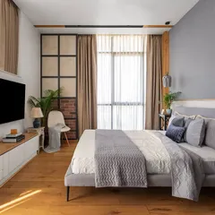 The master bedroom in Apartment 704 is a sanctuary of warmth and modern comfort. Wooden flooring, a cozy TV unit, and a mix of textures create a relaxing environment, with large windows providing ample daylight.