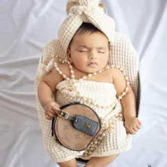 A touch of luxury for this little one. This sleeping newborn is styled with pearls and a designer-inspired bag for a unique and fashionable portrait.
