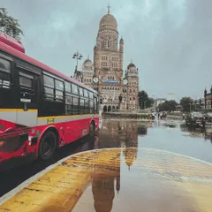 A classic red BEST bus adds a splash of color to a rainy day in front of the magnificent BMC building. The reflection in the puddle is the kind of detail that makes monsoon photography so special.