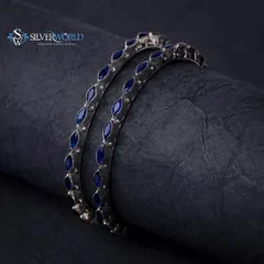 A pair of 92.5 silver bangles with rich blue enamel detailing. The dark, professional photography emphasizes the shine of the silver and the vibrant color, making them a standout accessory for any ethnic ensemble.
