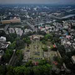 An aerial view of Shaniwar Wada in Pune, the historic seat of the Peshwas. The shot reveals the symmetrical layout of the gardens and foundations within the fort walls, nestled in the heart of the modern city.