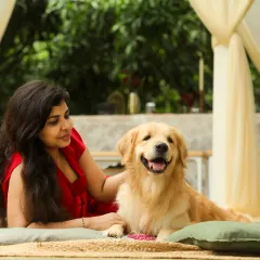 A woman in a red dress shares a happy moment with her Golden Retriever, relaxing together on a patio in a beautiful Bangalore setting.