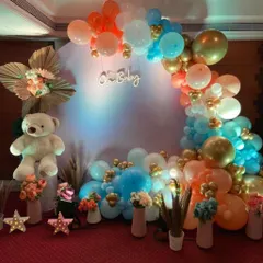 This vibrant baby shower setup features a fun color combination of blue, orange, and gold balloons. The design includes a large white teddy bear, an "Oh Baby" neon sign, and floral arrangements for a cheerful look.