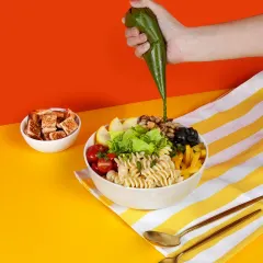 Our Pesto Piccolo bowl getting its final touch. A generous drizzle of fresh pesto dressing brings together the pasta, cherry tomatoes, and crisp greens for a truly energetic lunch.