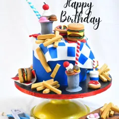 This fun illusion cake is designed to look like a classic American diner meal. It features an edible burger, fries, and a milkshake, all sculpted from fondant and cake, making for a truly surprising birthday treat.