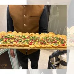 Our Papdi Chaat board is the life of the party. A server presents a long wooden board layered with crispy papdi, yogurt, chutneys, and fresh garnishes, ready to be shared.
