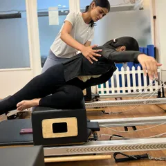 An instructor provides guidance on a back extension exercise on the reformer box during our teacher training program.