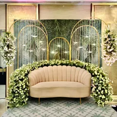 This intimate couple seating is part of my tropical rainforest theme. The setup features a shell-back sofa surrounded by white florals, with a backdrop of golden arches and hanging crystal birds.