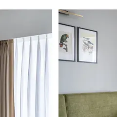 A composition of details: the soft fall of a curtain next to framed botanical art. This juxtaposition of soft textiles and structured frames creates a pleasing visual balance.
