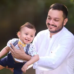 A happy father holding his smiling baby, who is dressed smartly in a bow tie and suspenders. This image showcases a mix of playful energy and sweet style.