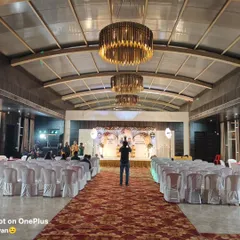 A wide shot of a banquet hall set up for a 25th birthday or anniversary celebration. I handle the stage decor, seating arrangements, and the overall lighting to create a grand and festive atmosphere.
