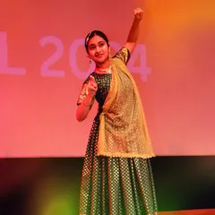 A solo performer strikes a confident pose during her classical dance segment at Pehal 2024. The stage lighting and traditional green and gold costume create a memorable moment.