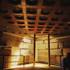 This image captures an interactive space defined by light and texture. The dramatic uplighting on the rough-hewn stone walls and the shadows cast by the filler slab ceiling create an atmosphere of warmth and mystery.
