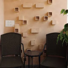 A cozy balcony corner designed for quiet moments. The textured wall with sculptural niches, patterned floor tiles, and woven chairs create a space that is rich in detail and character.