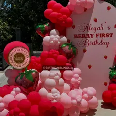 A close-up of a "Berry First Birthday" balloon arrangement, featuring shades of pink and red with strawberry-shaped foil balloons.