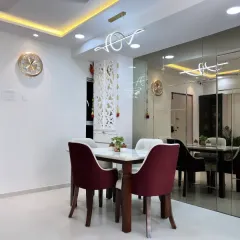 The dining area adjacent to the living room, featuring plush velvet chairs and a mirrored wall that enhances the sense of space and light. The elegant chandelier adds a final touch of sophistication.
