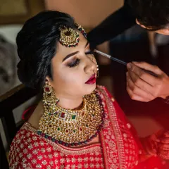 The makeup artist applies the finishing touches to the bride's eyes. This close-up shot highlights the artistry and focus involved in creating the perfect bridal look.