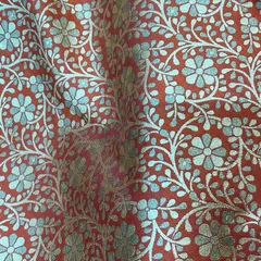 A close-up of a luxurious red brocade fabric with a silver and blue floral vine pattern. This material is ideal for a groom's sherwani or a statement wedding jacket.