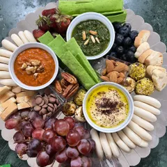 A vibrant grazing board perfect for intimate gatherings. It features a trio of my signature dips: classic hummus, spicy muhammara, and fresh pesto, served with a variety of crackers, breads, fruits, and nuts.